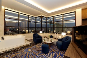 A modern hotel room with a large window, a bathtub, a sofa, and a round coffee table.