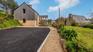 Una calle residencial con calzada pavimentada, entrada de grava y casas con fachadas de piedra y madera.