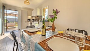 Un comedor con una mesa dispuesta para cuatro personas, una botella de vino y un jarrón con flores.