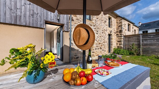 Un área de comedor al aire libre con una mesa lista para una comida, una cesta de frutas y una planta en maceta.