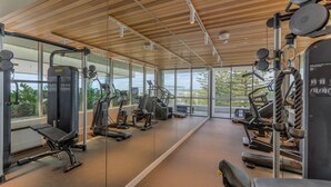Ein Fitnessraum mit verschiedenen Trainingsgeräten, großen Fenstern und einer Holzboden.