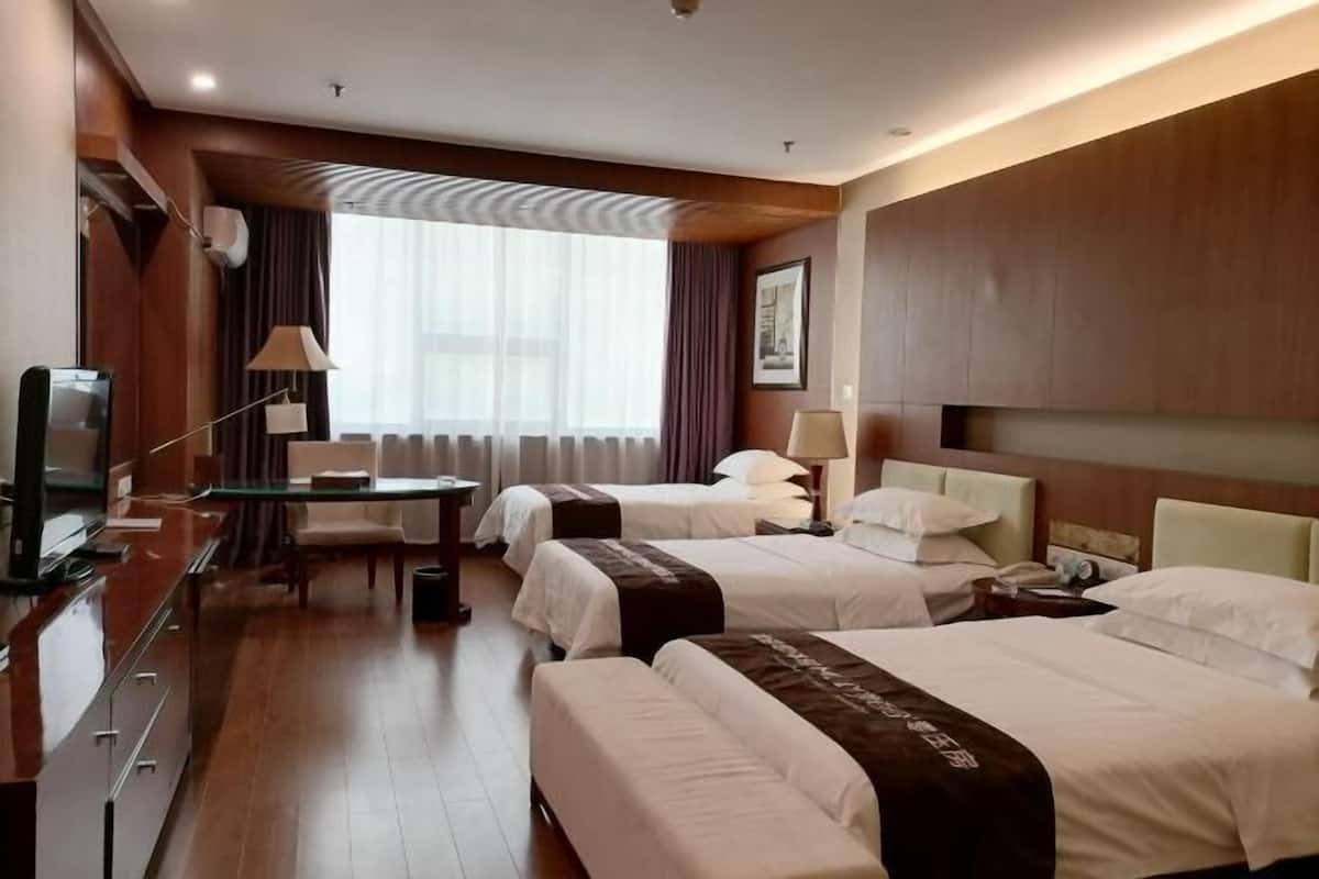 Une chambre d’hôtel avec deux lits, un bureau, une chaise, une télévision et une fenêtre avec des rideaux.