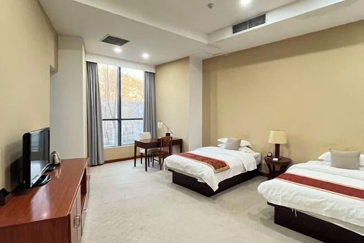 Une chambre d’hôtel avec deux lits, un bureau avec une chaise, une télévision et une grande fenêtre avec des rideaux.