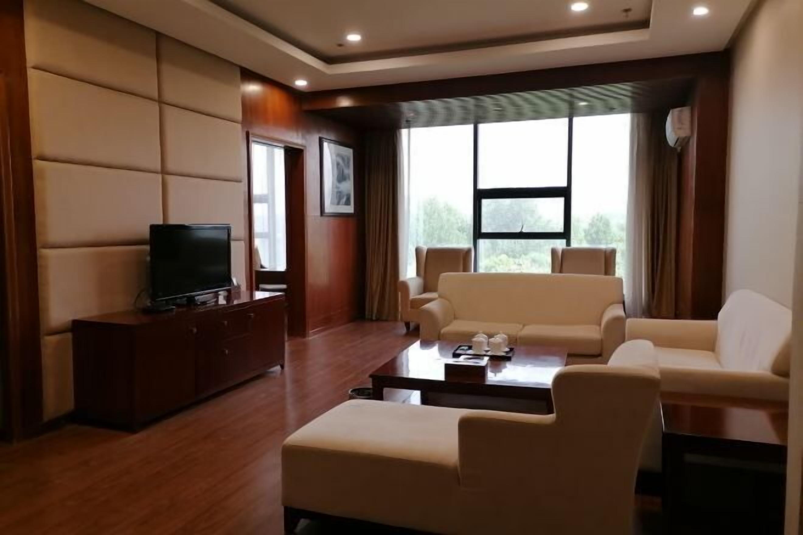 A modern living room with a flat-screen TV, a sofa set, a coffee table, and a large window with curtains.