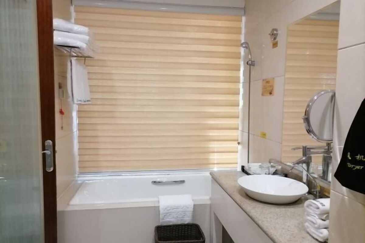Un baño con bañera, lavabo, espejo y ventana con persianas.