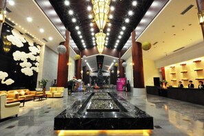 Un vestíbulo de hotel con un mostrador de recepción de mármol, asientos elegantes, una fuente y una araña.