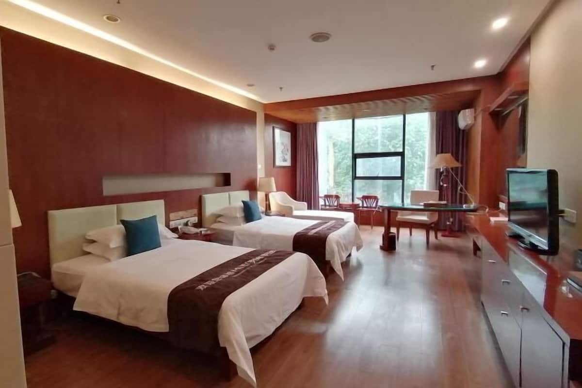 Une chambre d’hôtel avec deux lits, un bureau, une chaise, une télévision et une grande fenêtre.