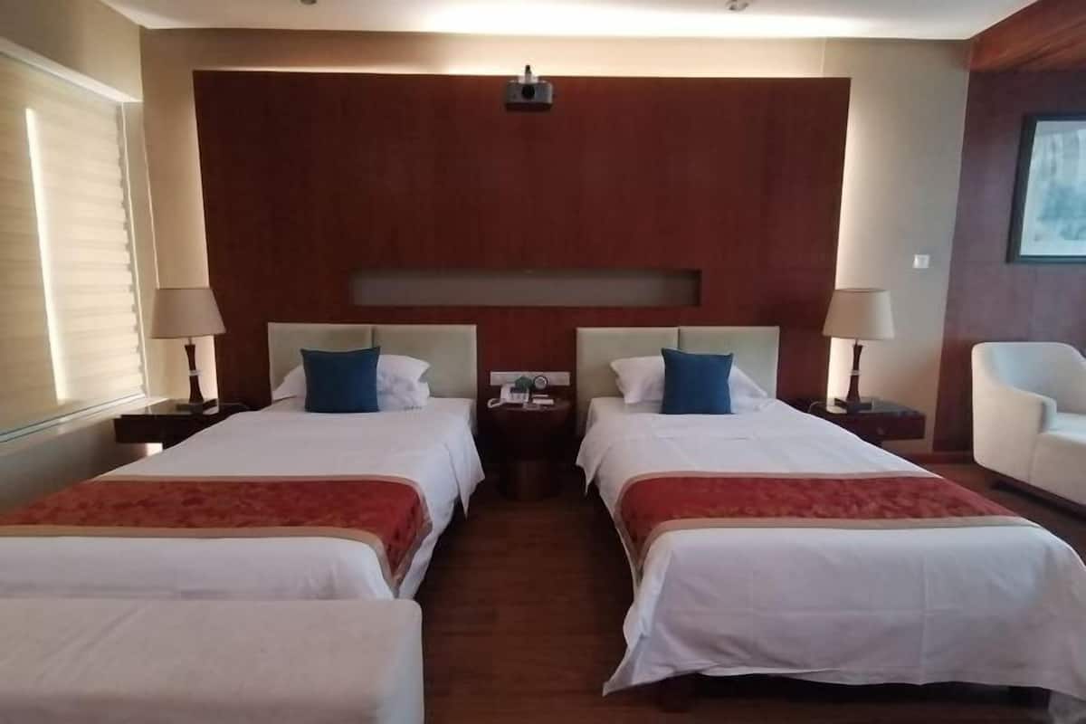 Une chambre d’hôtel avec deux lits, une tête de lit en bois, une petite table avec une lampe et une chaise.