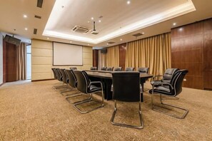 Een vergaderzaal met een lange tafel, meerdere stoelen, een scherm voor een beamer en een vloerbedekking.