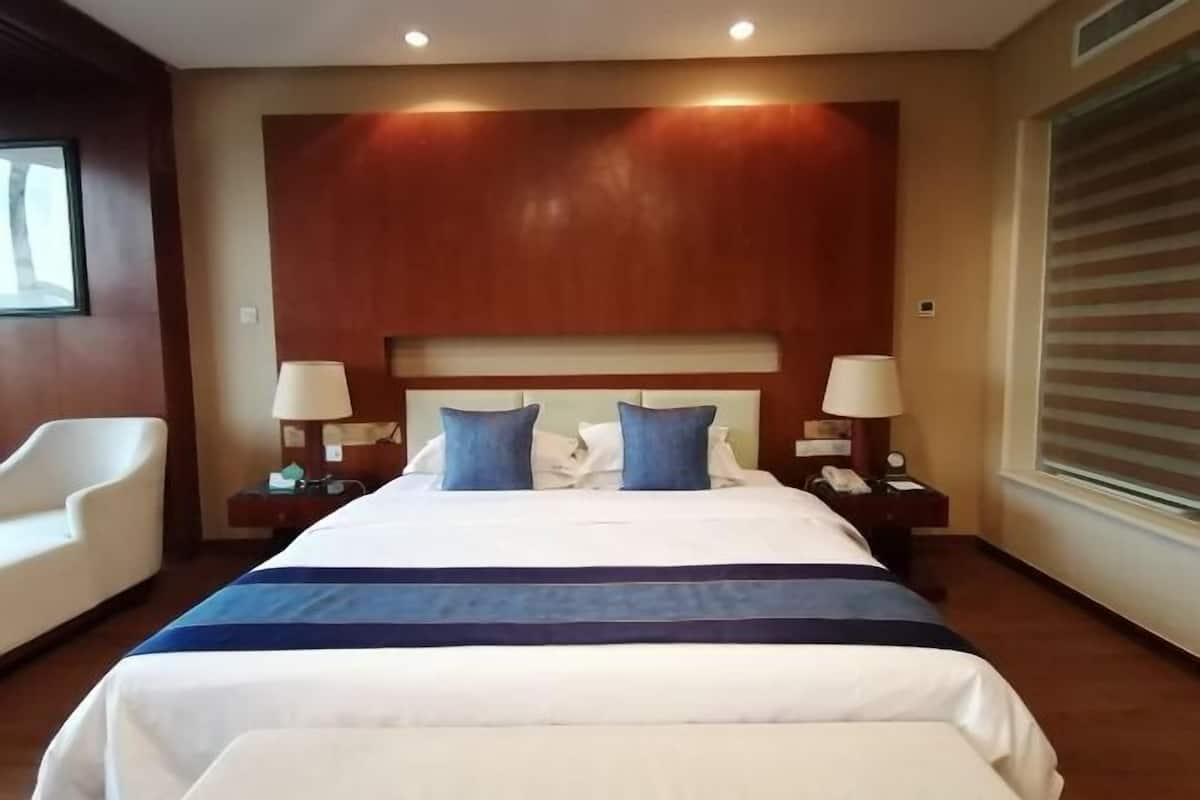 Une chambre d’hôtel avec un grand lit, deux tables de chevet avec des lampes, une chaise et une fenêtre avec des stores.