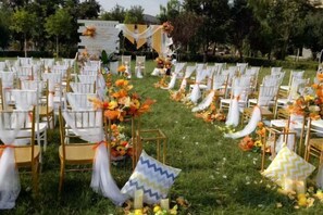 Un espacio al aire libre para eventos, con filas de sillas y mesas, decorado con arreglos florales y detalles textiles.