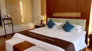 Habitación de hotel con una cama grande, una mesita de noche con lámpara, un cabecero de madera y una ventana con persianas.