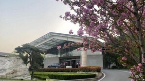 A modern building with a glass facade, a large rock feature, and a curved driveway. - Bei Long Garden Hotel (Qingzhou)
