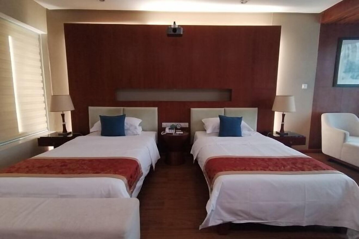 Una habitación de hotel con dos camas, cabecero de madera, una mesita y una silla.