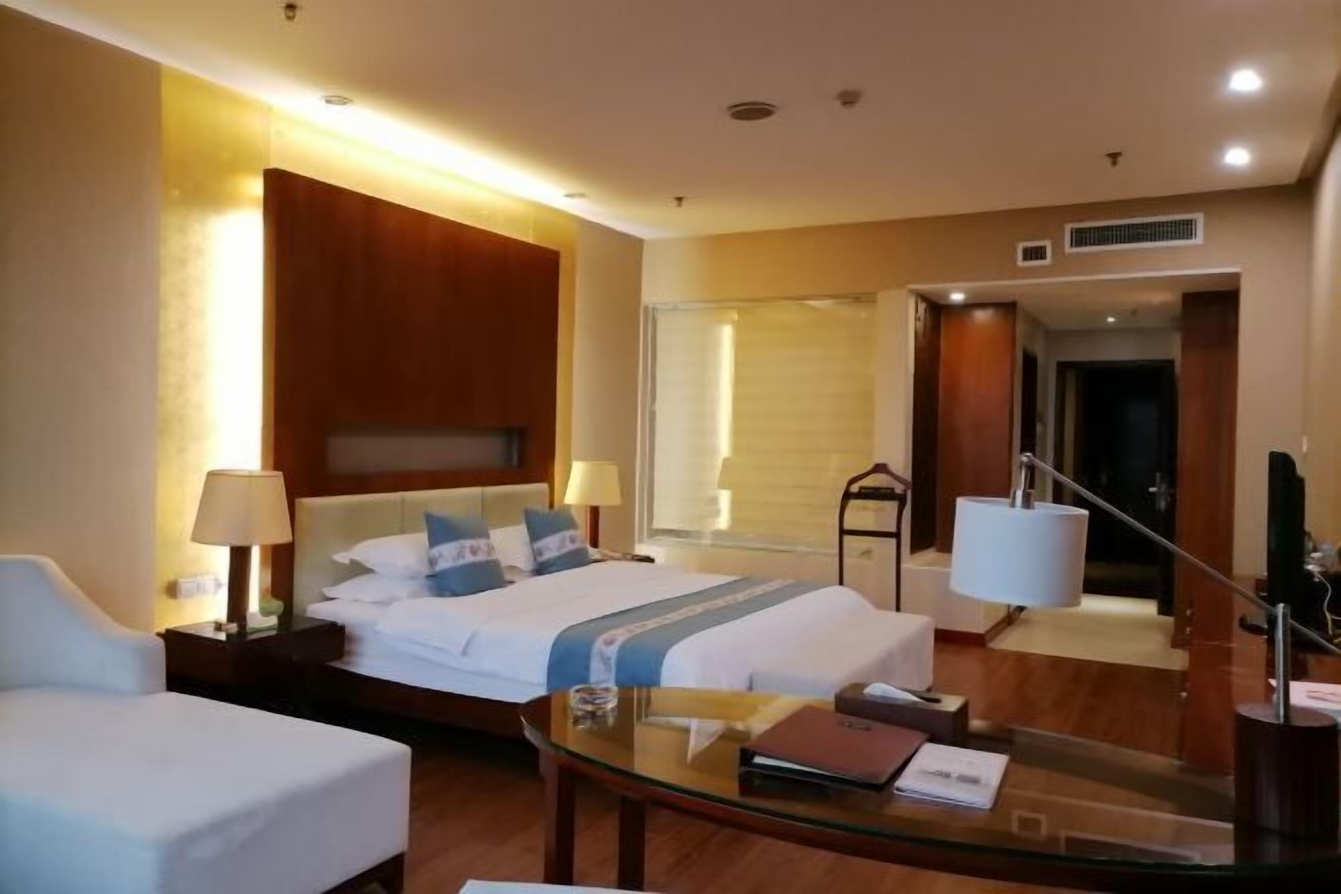 A hotel room with a bed, a desk, a chair, a lamp, and a mirror.