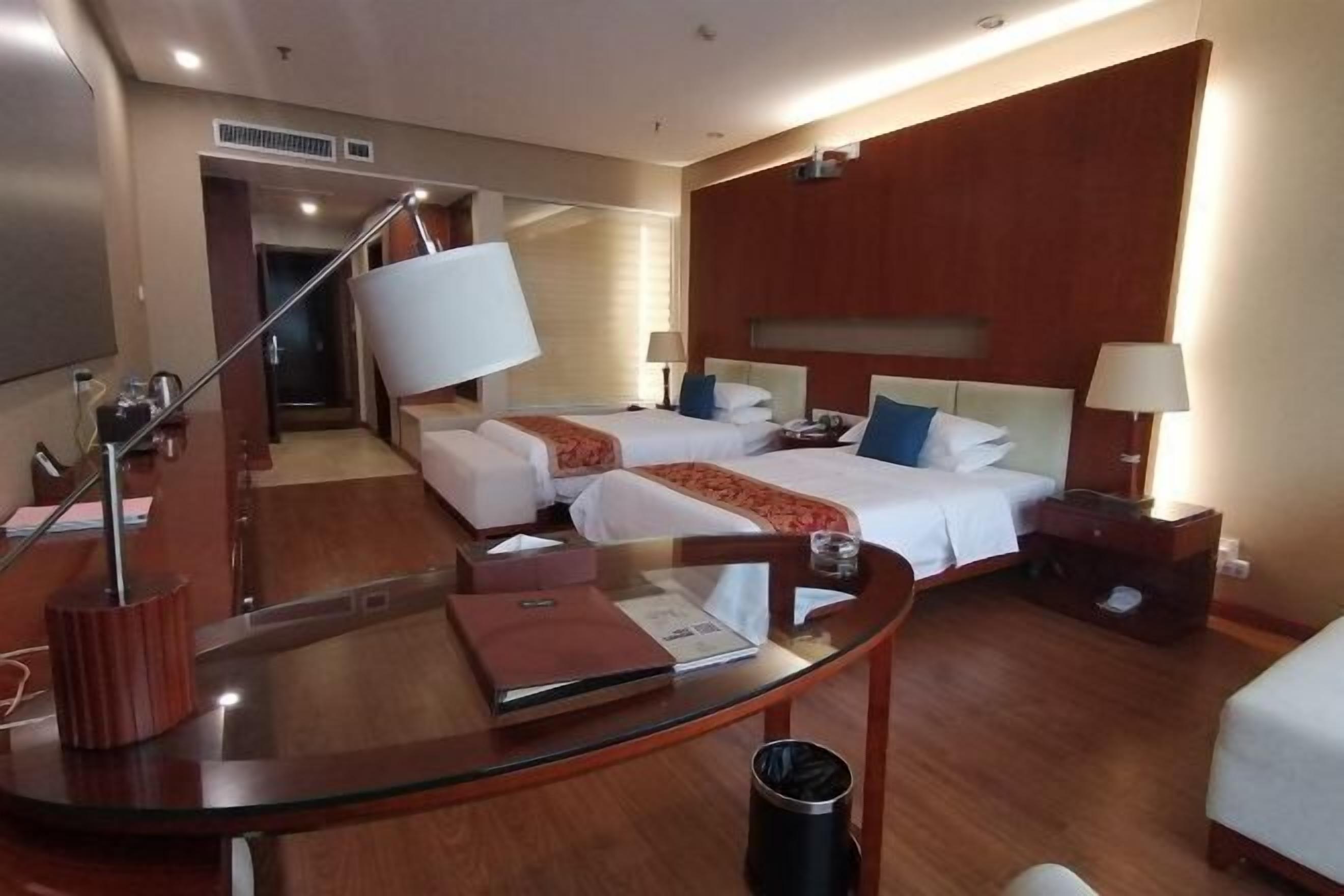 Une chambre d’hôtel avec deux lits, une table en verre, un bureau, une lampe et une poubelle.