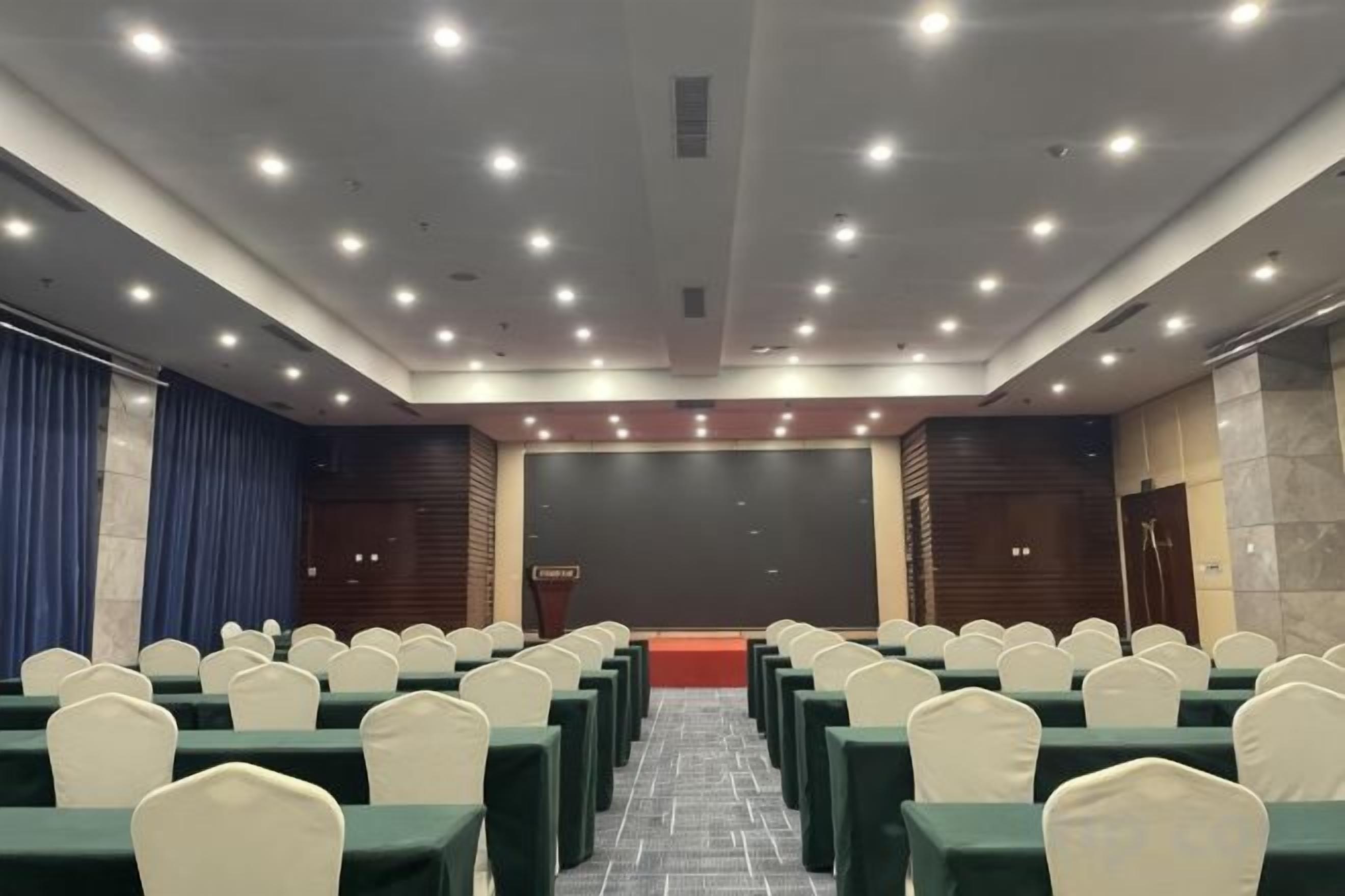 A conference room with rows of chairs, a stage, and a large screen.
