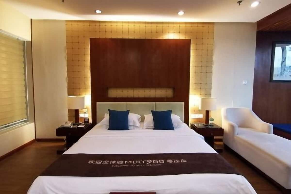 Une chambre d’hôtel avec un grand lit, deux tables de chevet avec des lampes, un fauteuil blanc et une tête de lit en bois.