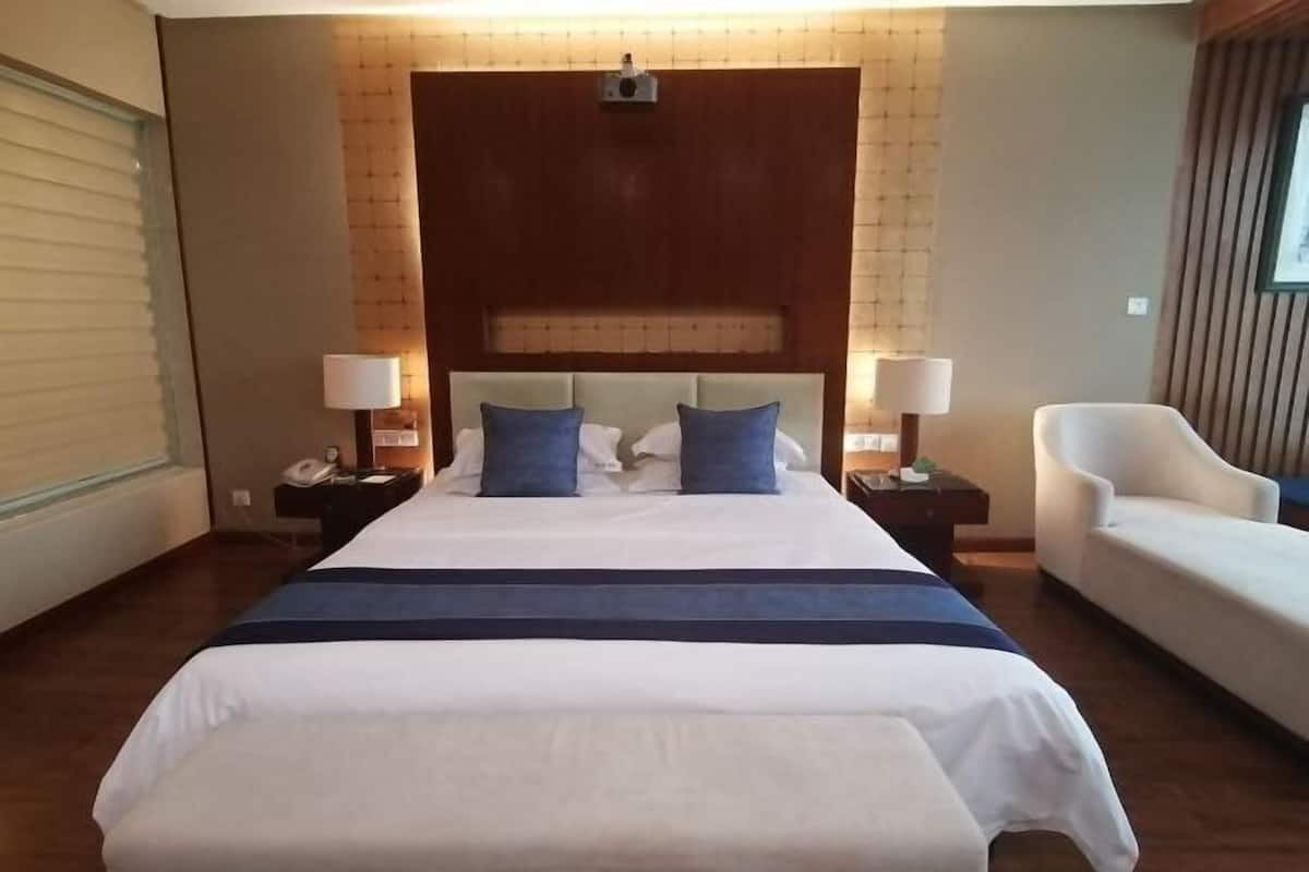 Une chambre d’hôtel avec un grand lit, deux tables de chevet avec des lampes, une chaise et une tête de lit intégrant un téléviseur.