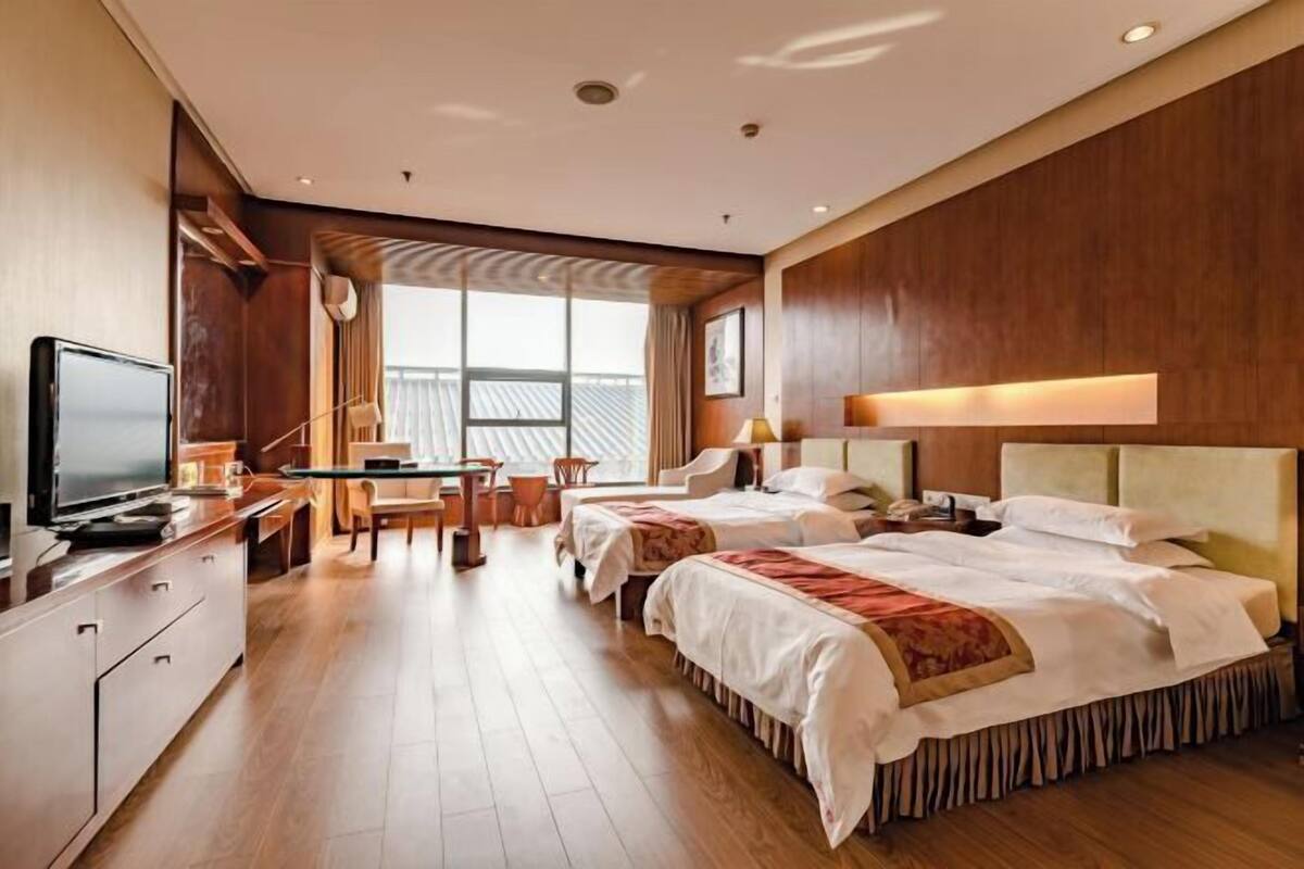 Une chambre d’hôtel avec deux lits, un bureau, une télévision et une grande fenêtre.