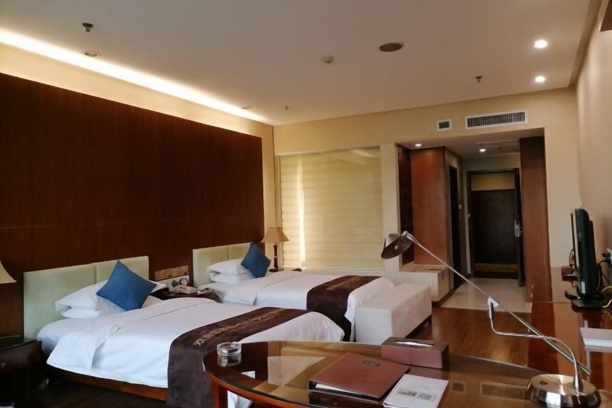 Una habitación de hotel con dos camas, un escritorio con lámpara, televisión y ventana con persianas.