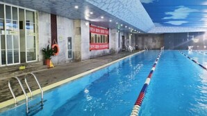 An indoor swimming pool with clear lane dividers, a tiled ceiling, and a red banner on the wall. - Bei Long Garden Hotel (Qingzhou)