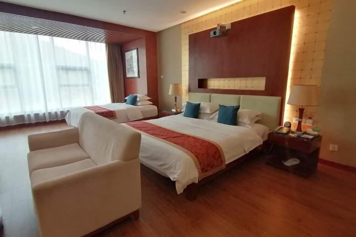 Une chambre d’hôtel avec deux lits, un canapé, une table de chevet avec une lampe et une fenêtre avec des rideaux.