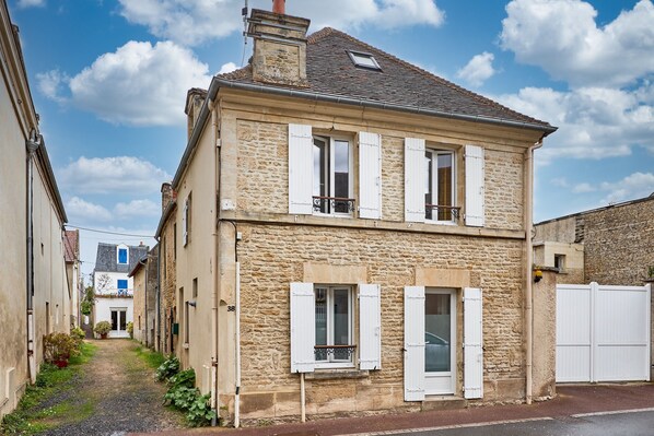 A two-story stone building with white shutters, a visible number '38', and a narrow alleyway.