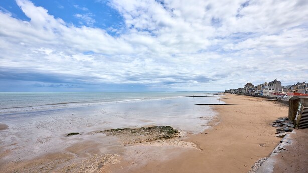 A beach with a clear sky, calm sea, and buildings along the shore.