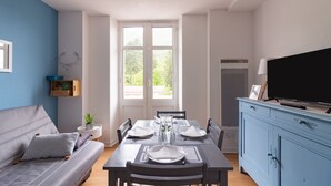 A dining area with a table set for four, a sofa, a TV, and a window with a view of trees.