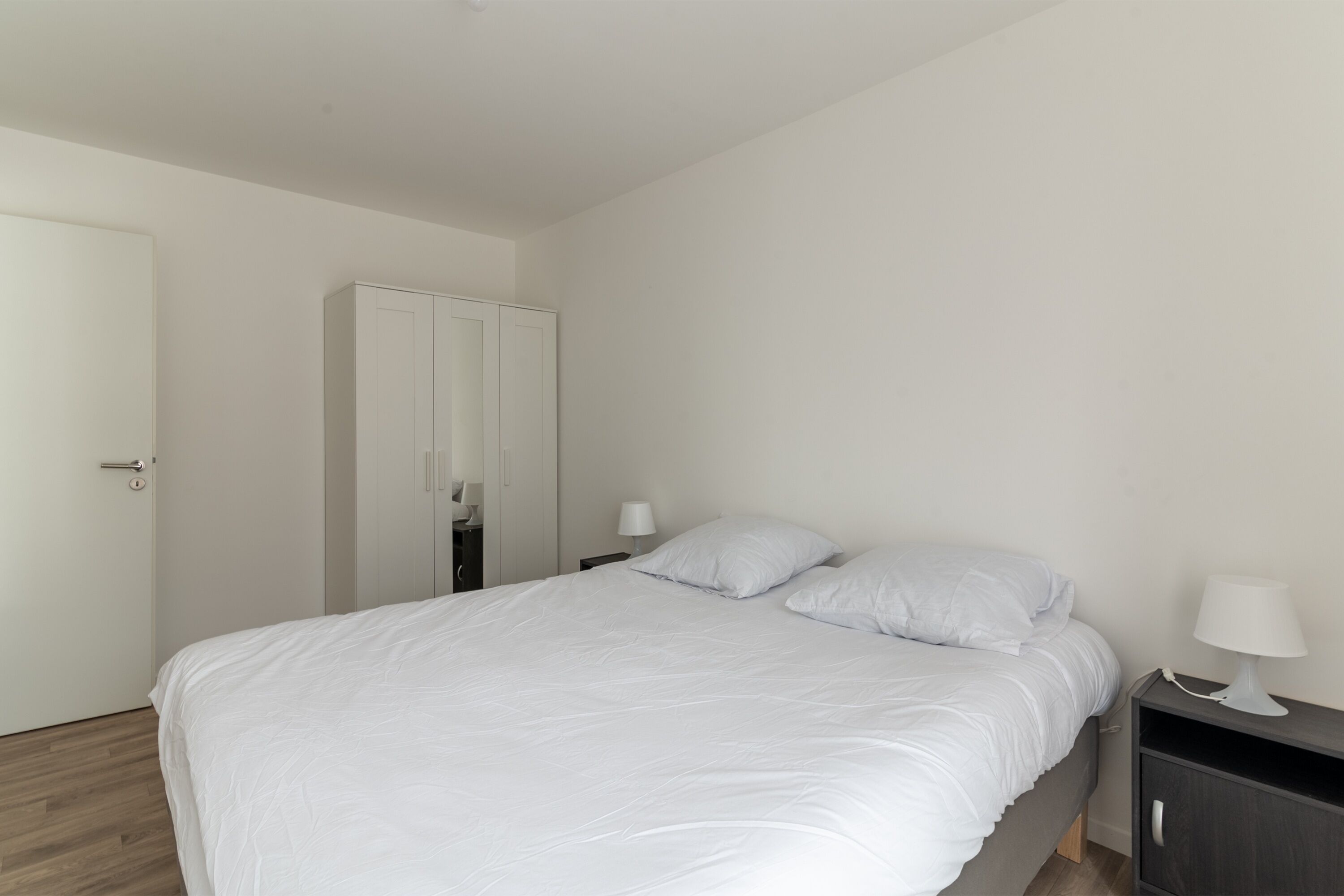 Une chambre à coucher avec un lit, une table de chevet, une armoire et une porte.