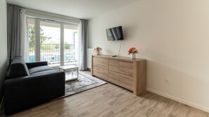 Un salon moderne comprenant un canapé, un meuble en bois, un téléviseur à écran plat et une grande porte-fenêtre coulissante donnant sur un espace extérieur.