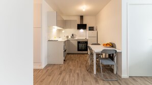 Une cuisine compacte avec des meubles blancs, un four à micro-ondes, une cuisinière et un coin repas comprenant une table et des chaises.