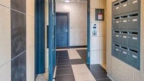 Un couloir avec un sol à carreaux, une porte et une rangée de boîtes aux lettres sur le côté droit.