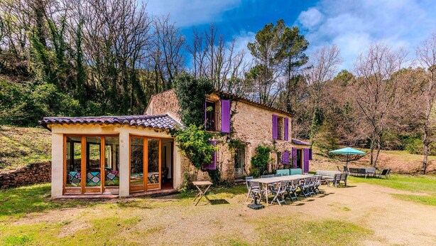Una casa de piedra rústica con un patio acristalado y zona de estar exterior.
