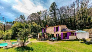 Una casa de piedra con persianas moradas, piscina y mobiliario de exterior.