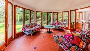 Una habitación soleada con ventanas amplias, piso de baldosas rojas y sofás coloridos con diseños.