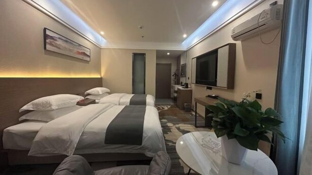 A modern hotel room with a bed, bedside table, and a potted plant.