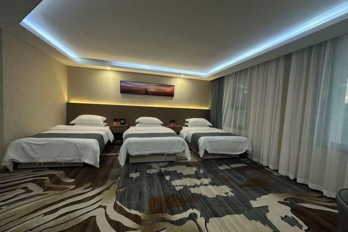A hotel room with three beds, a large rug, a flat-screen TV, and a large window with curtains.