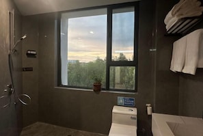 A bathroom with a large window, a toilet, and a shower area. - Shenhe Hotel (Habahe)