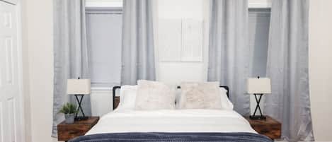 A bedroom with a bed, two bedside tables with lamps, and grey curtains.