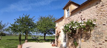 Um edifício de pedra com jardim, pérgola e vista para o campo.