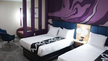A hotel room with a large bed, a desk, a chair, and a purple accent wall.