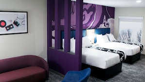 A hotel room with two beds, a red sofa, a blue chair, and a purple partition.