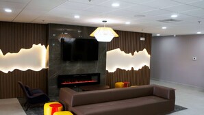 A modern lobby with a sofa, ottomans, a flat-screen TV, and a fireplace.