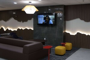 Un área de estar moderna con un sofá, dos otomanas amarillas, una mesa roja y un televisor montado en la pared.