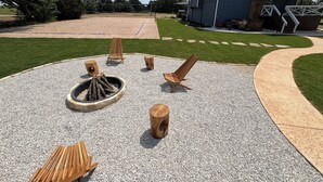 Eine Terrasse mit Sitzgelegenheiten im Freien, einer Feuerstelle und einem Haus im Hintergrund.