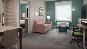 A hotel room with a sofa, a desk, a chair, a TV, and a window with blinds. - Home2 Suites By Hilton Georgetown Austin North (Georgetown)
