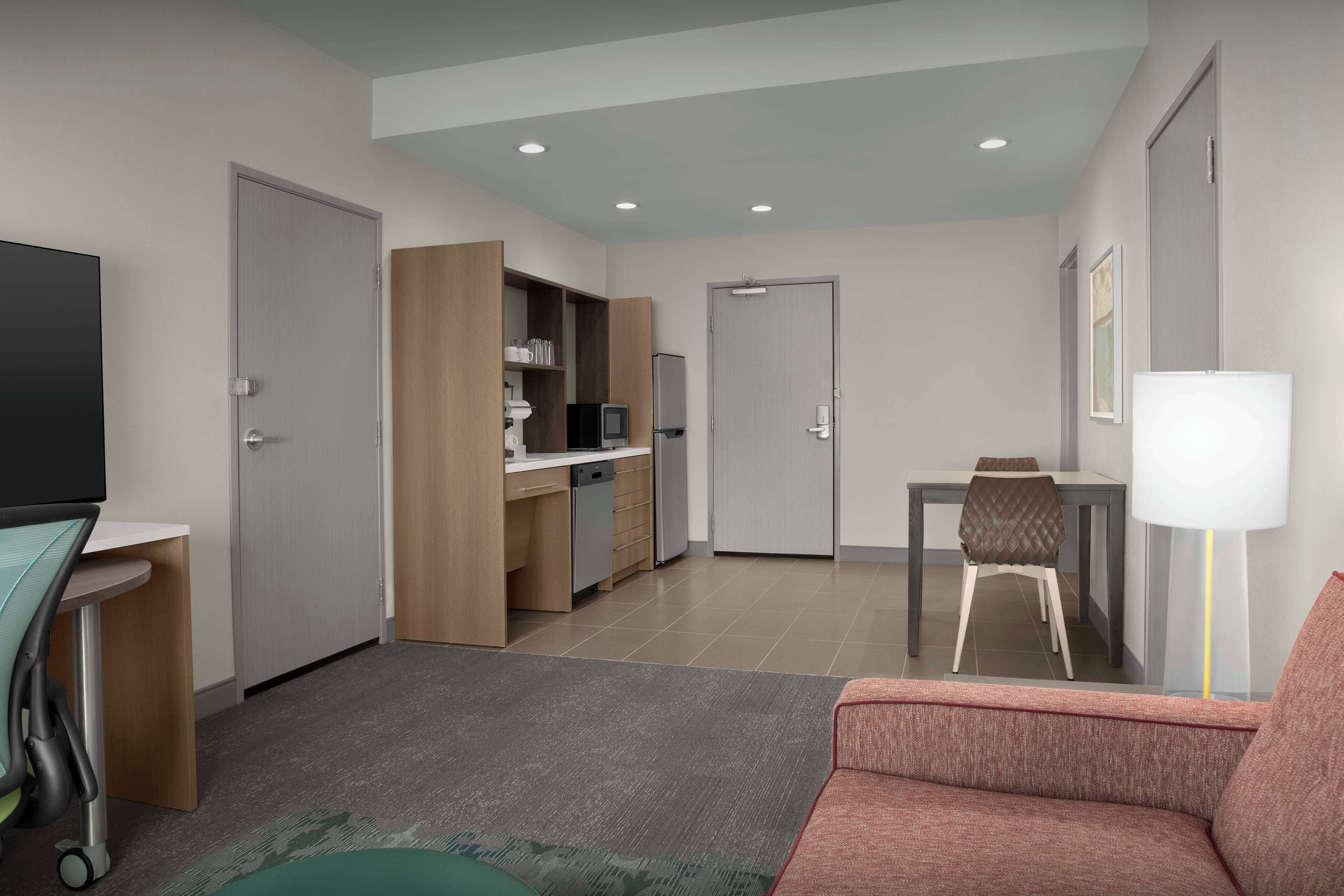 A modern living room with a sofa, a television, a desk, and a dining area with a chair and table.