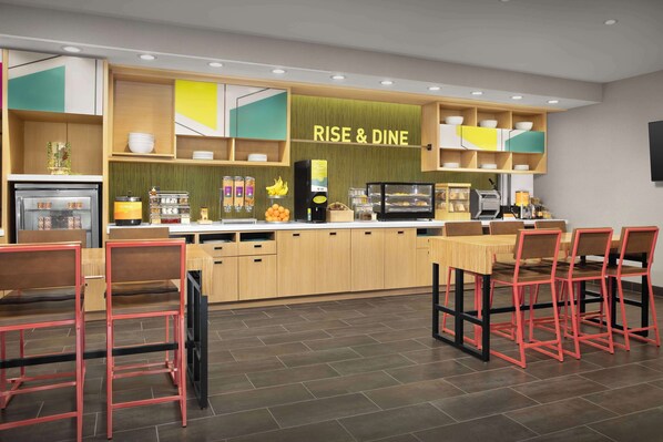Una cocina moderna con un letrero 'RISE & DINE', armarios de madera, una cafetera y sillas rojas.